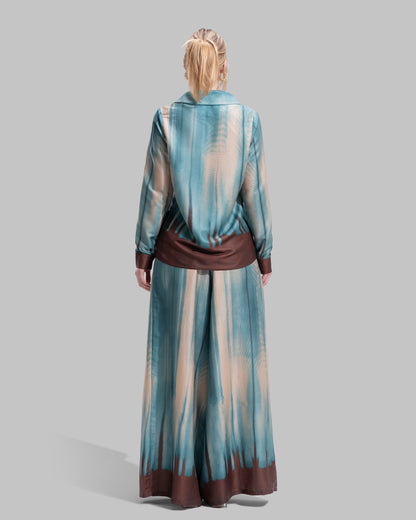 A long-sleeved button-down shirt featuring a teal and cream gradient print with a dark brown hem.